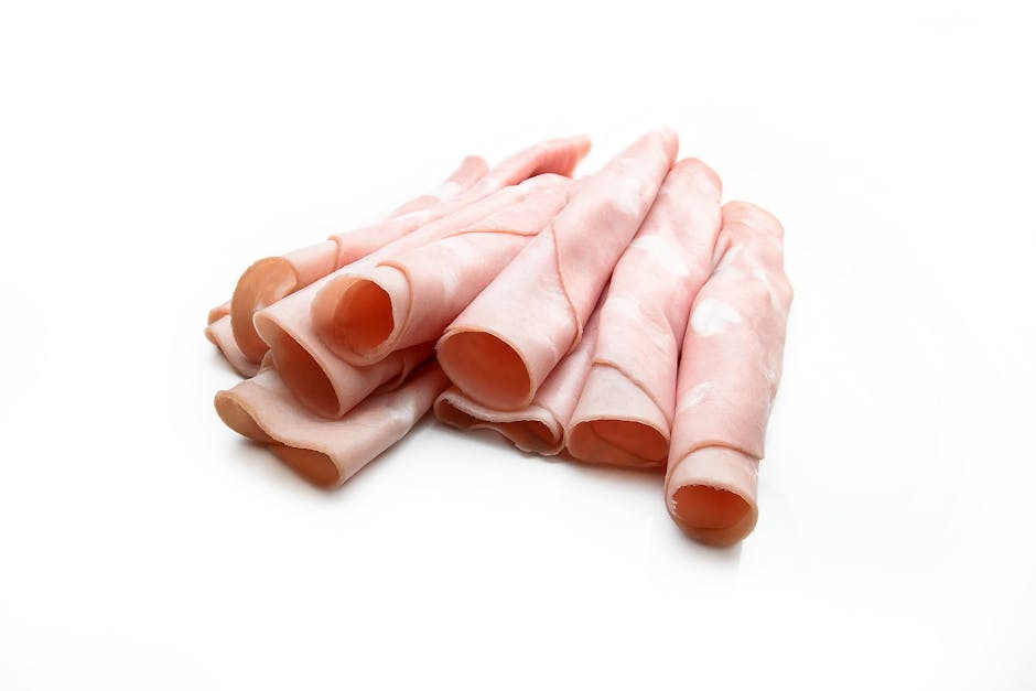 A close-up view of several raw chicken fillets with pale pink flesh and smooth texture, wrapped in transparent plastic wrap, resting on a white surface. The chicken pieces are irregular in shape and size, arranged in a slightly overlapping manner. In the background, there is a glimpse of a doorway leading into a room with a wooden floor. Some cardboard boxes and packing materials are visible, indicating a home relocation or moving process. The image emphasizes the preparation or packing of perishable food items during furniture transport or packing and moving activities, with natural lighting highlighting the details of the chicken and the surrounding environment, which includes elements associated with house removals, such as boxes and transportation of household items. Man with Van Ham offers professional removals services, including packing and move logistics.